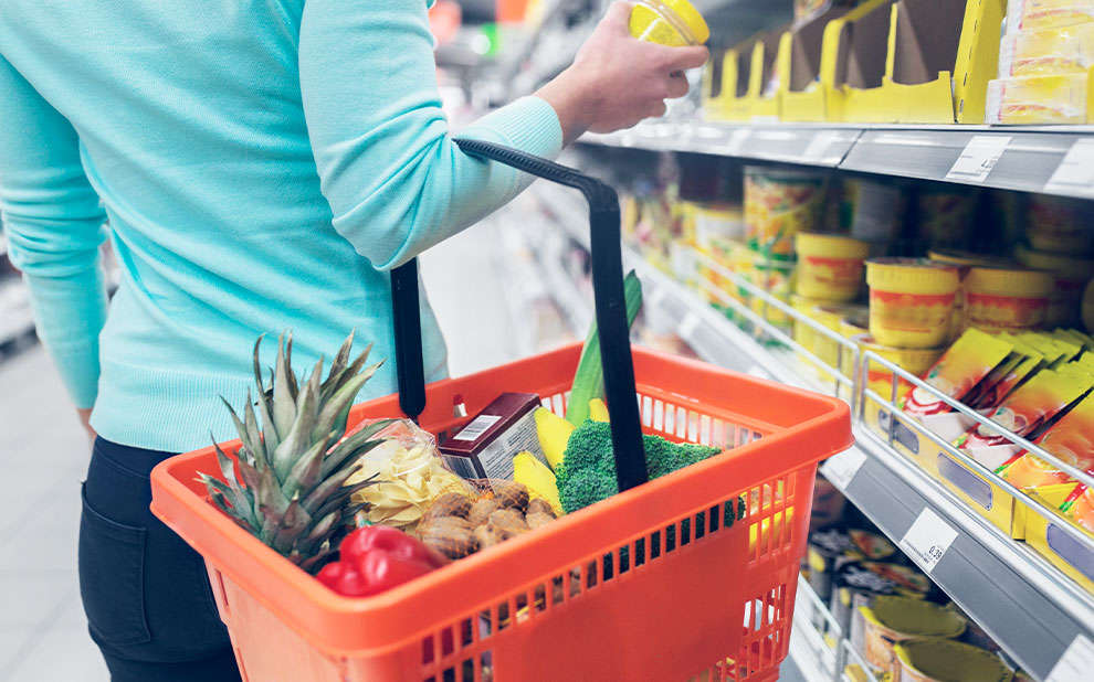 Mulher com cesta de frutas no braço em supermercado. 