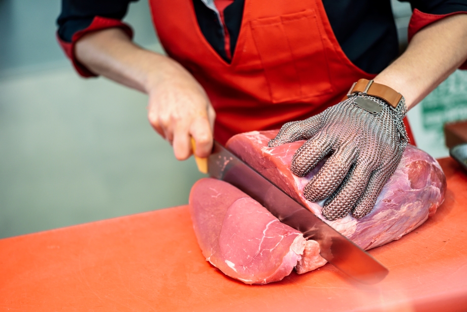 Imagem de homem cortando a carne. Ele usa uma luva de metal para proteger a mão do corte.