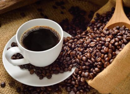 Imagem de um copo de café ao lado tem grãos torrados.